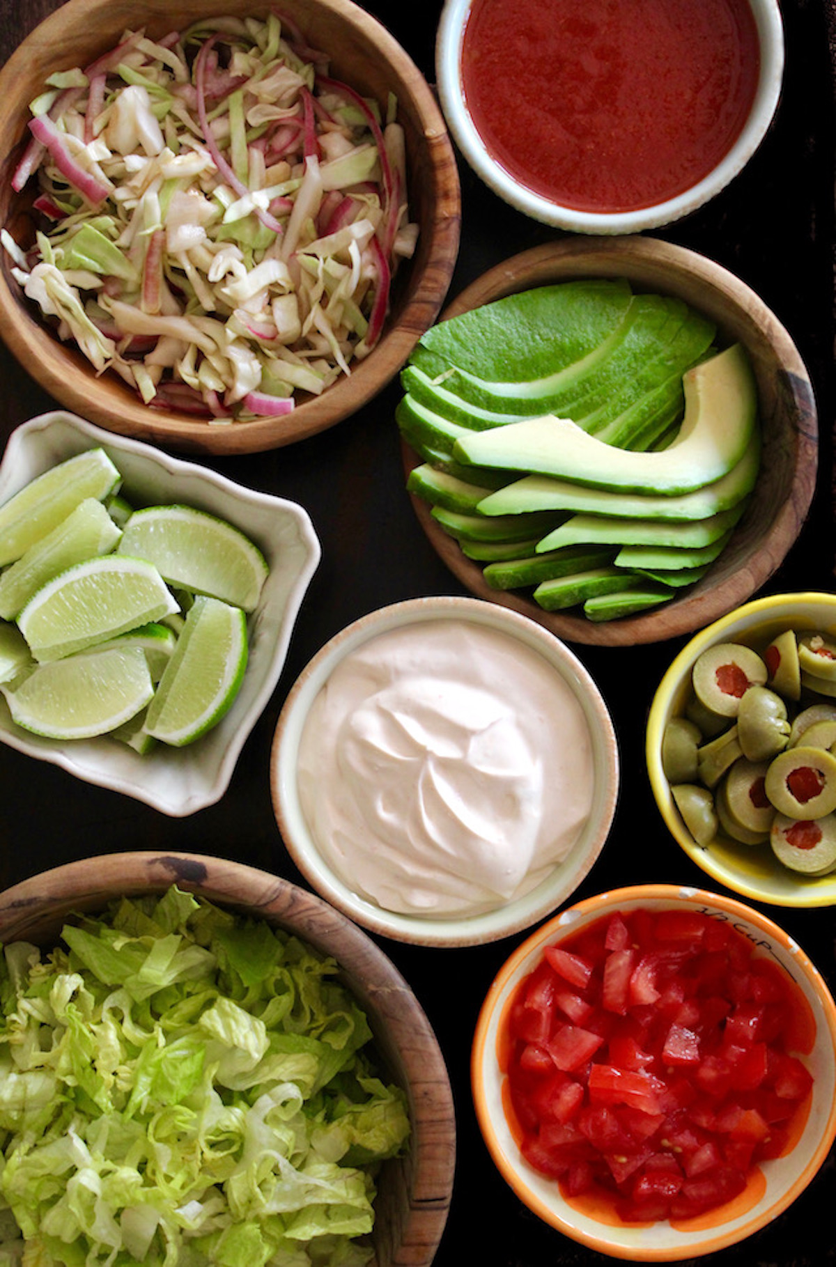 All of the filling for tacos in bowls - limes, slaw, avocados, sour cream, tomatoes and lettuce.