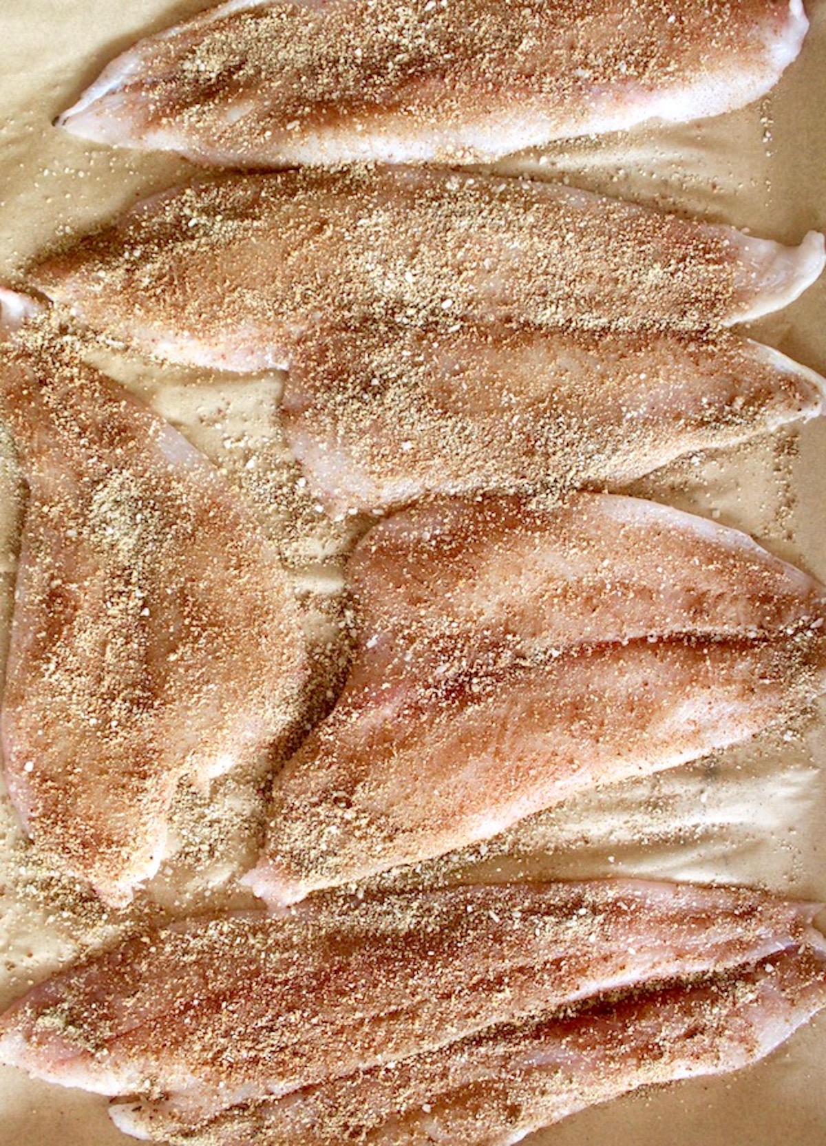 Raw sole fillets with spice mix on top on parchment paper.