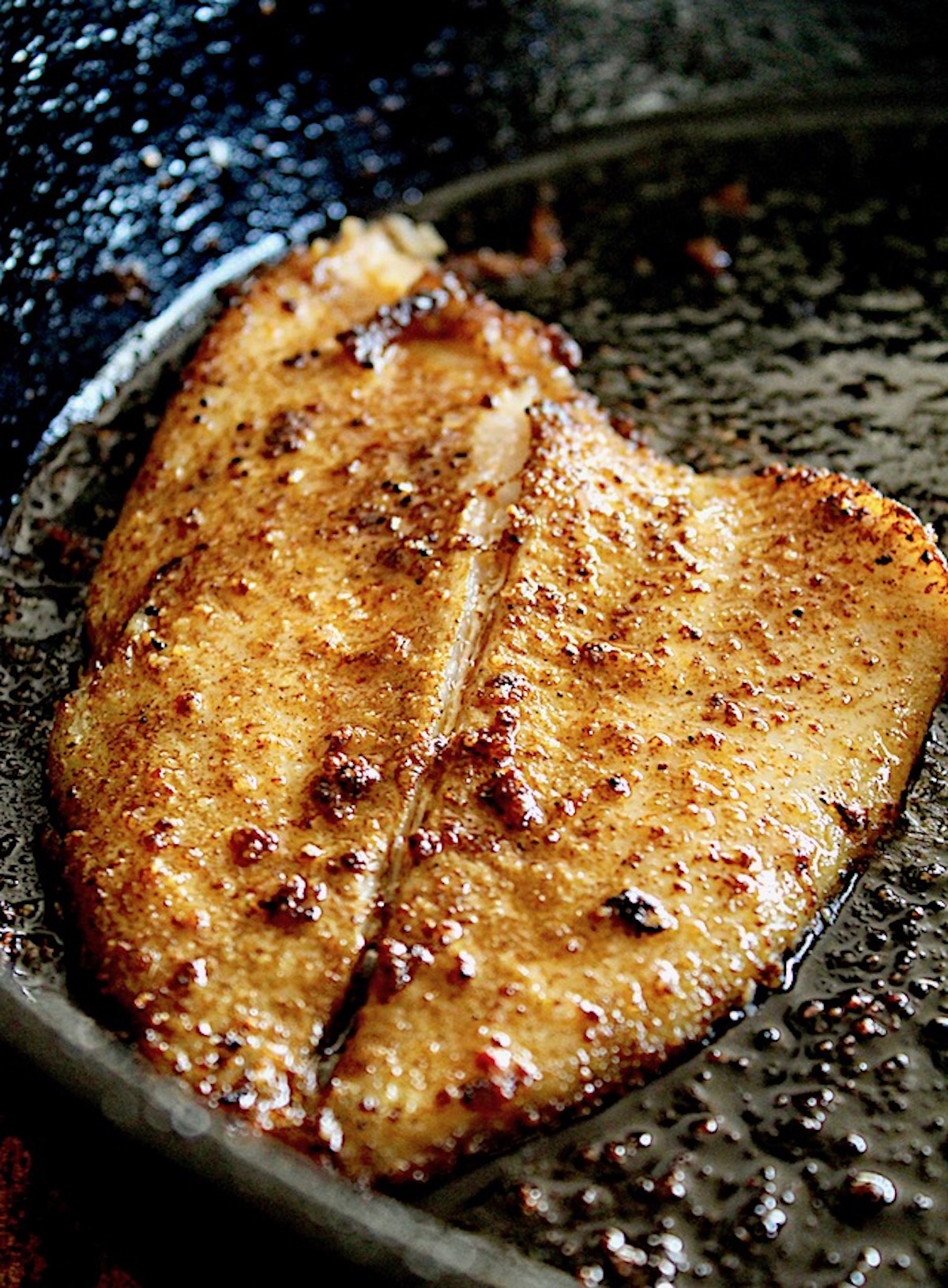 A large fillet of sole in cast iron skillet with spices.