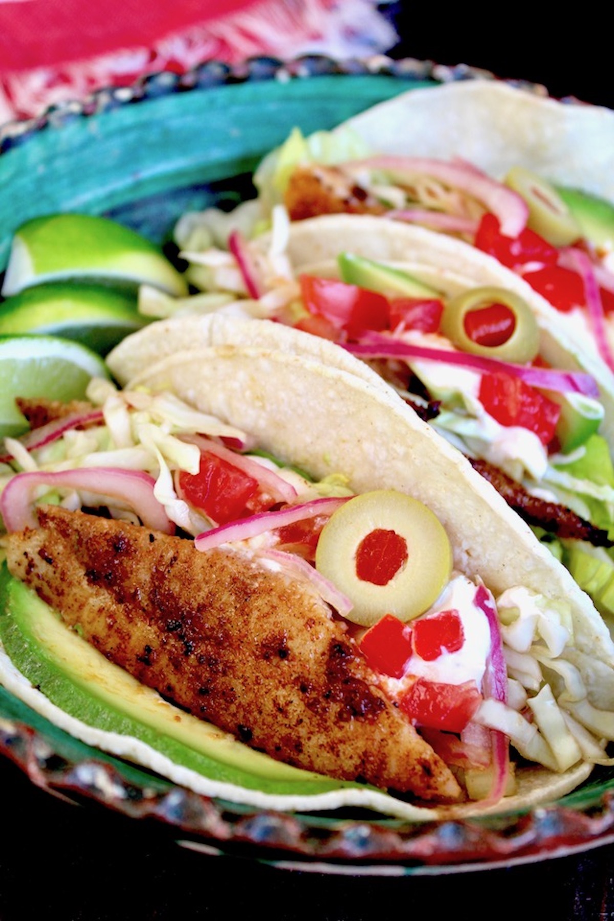 Three blackened fish tacos in a blue dish with alvoado and lime slices.