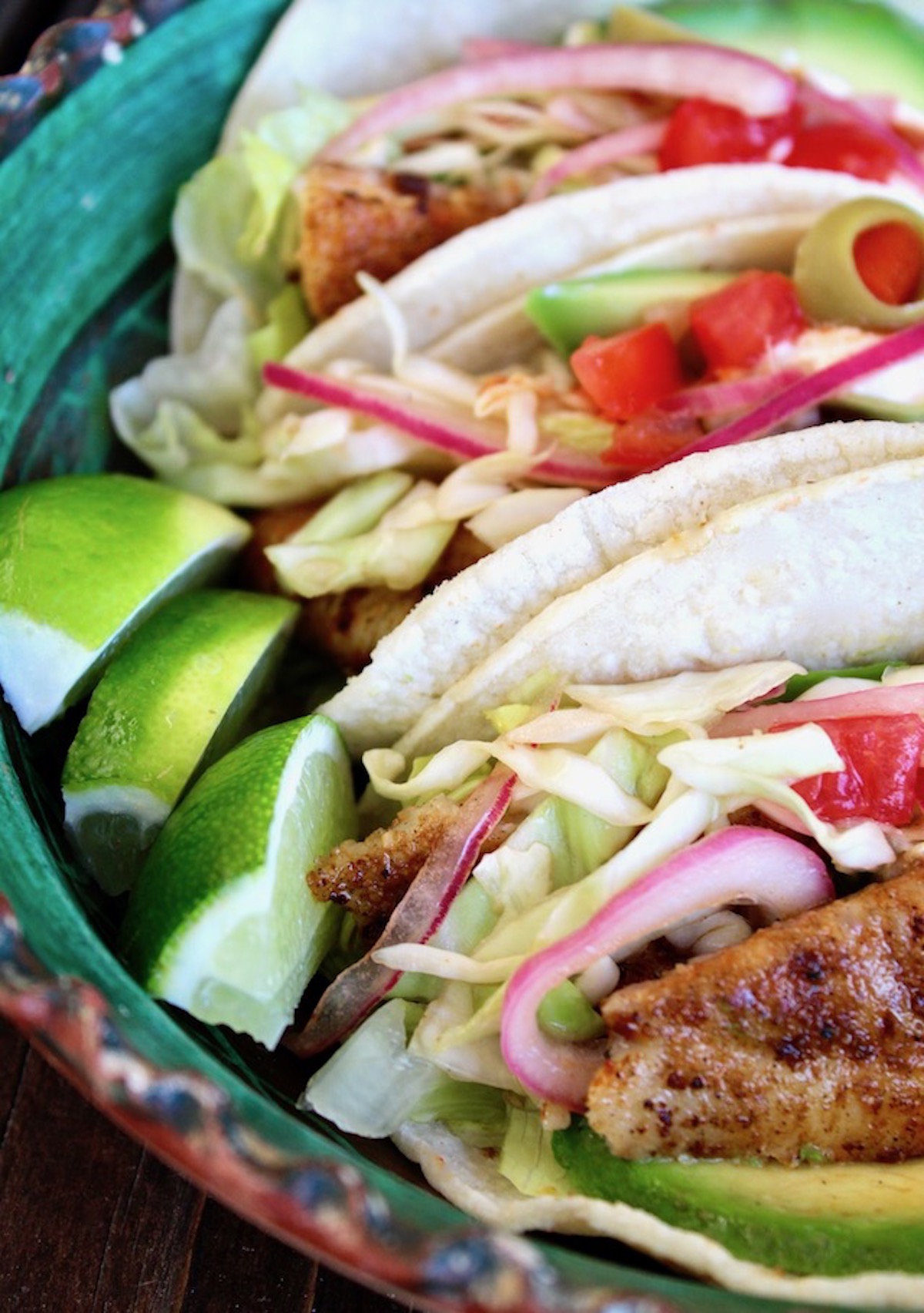 Close up of fish tacos with 3 wedges of lime.