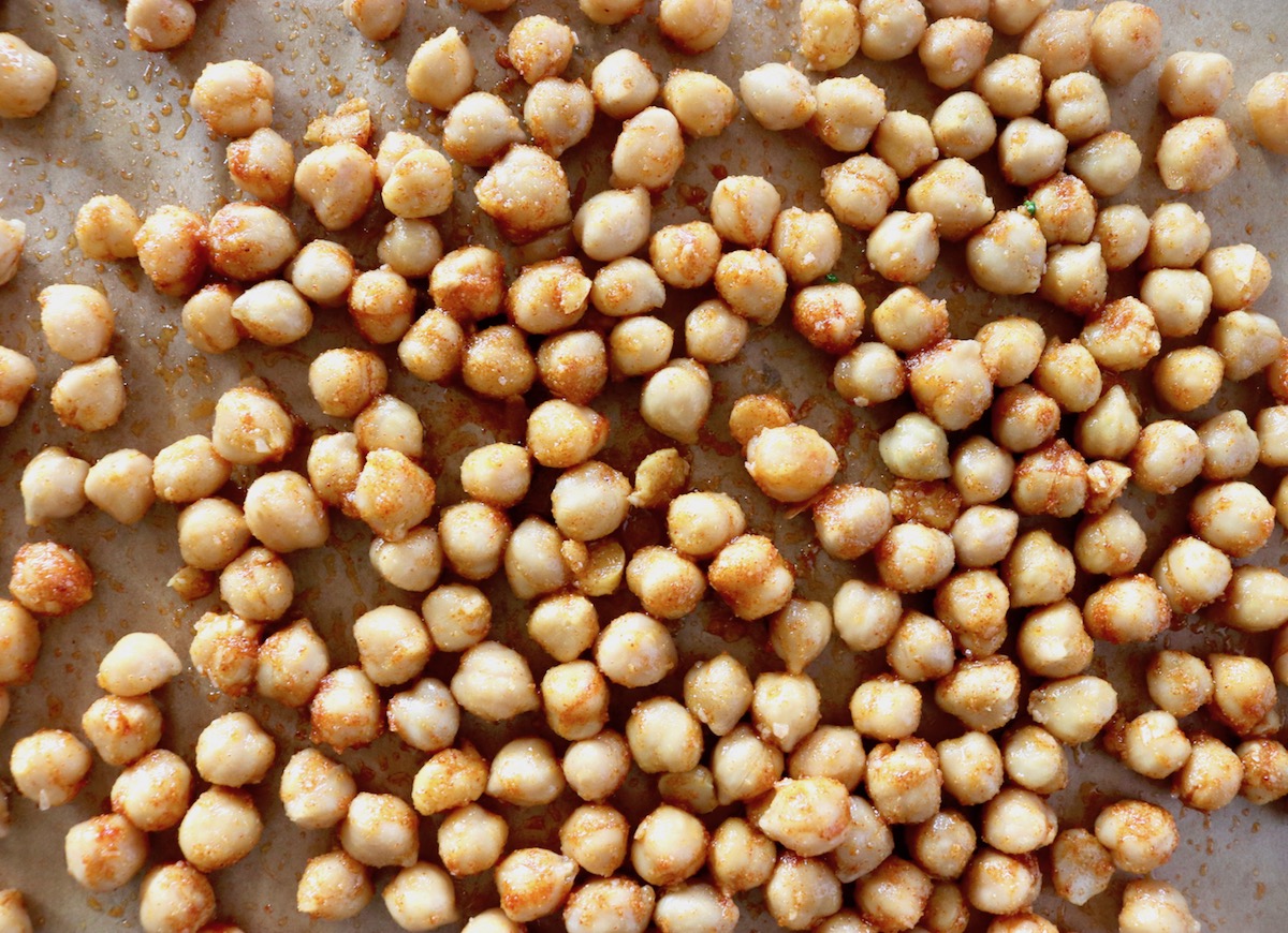 Raw garbanzo beans with oil and spices on a parchment-lined baking sheet.