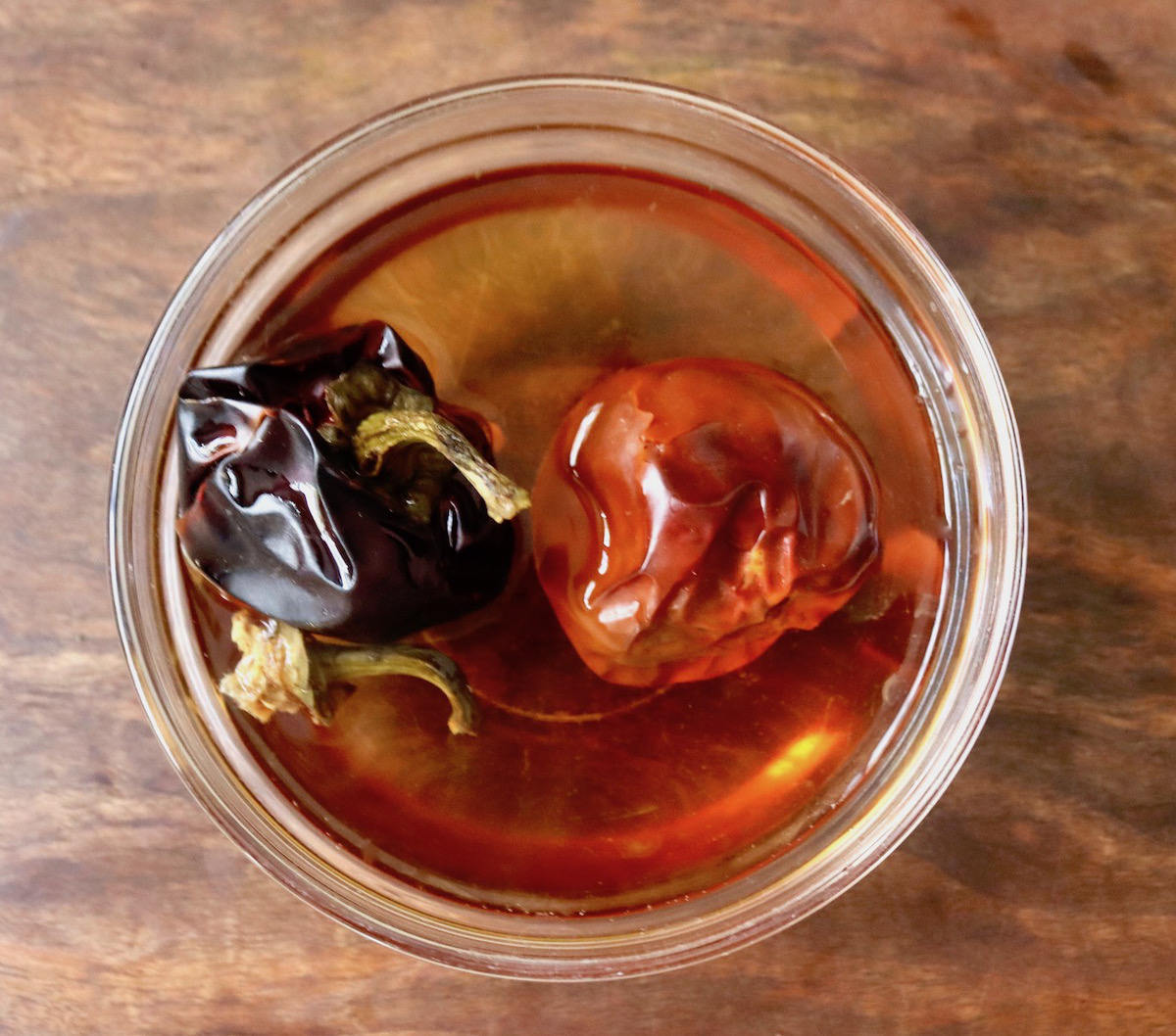 Small glass bowl with water and two dark red dried pepper.
