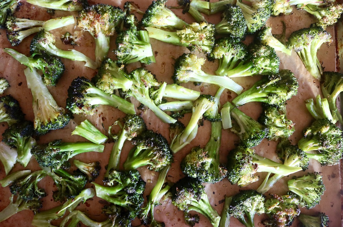 Charred pieces of broccoli on a parchment-lined baking sheet.