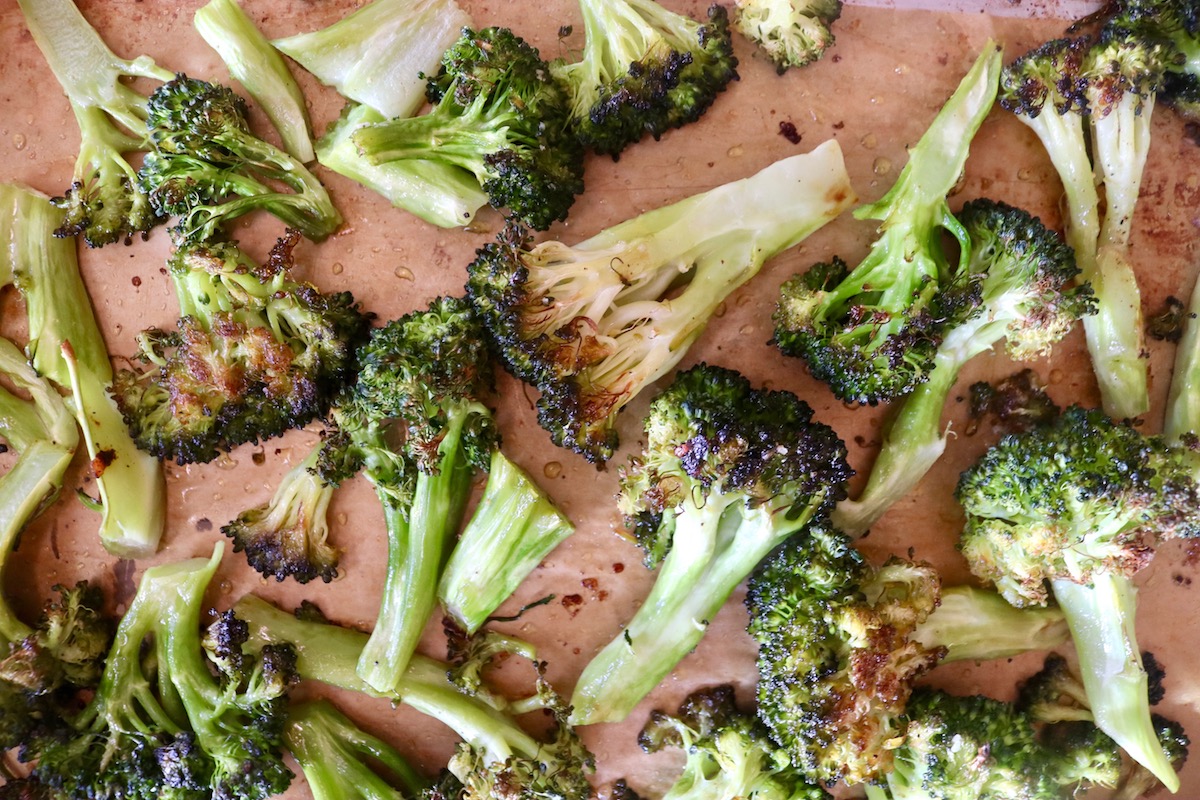 Several charred broccoli florets on a parchment-lined baking sheet.