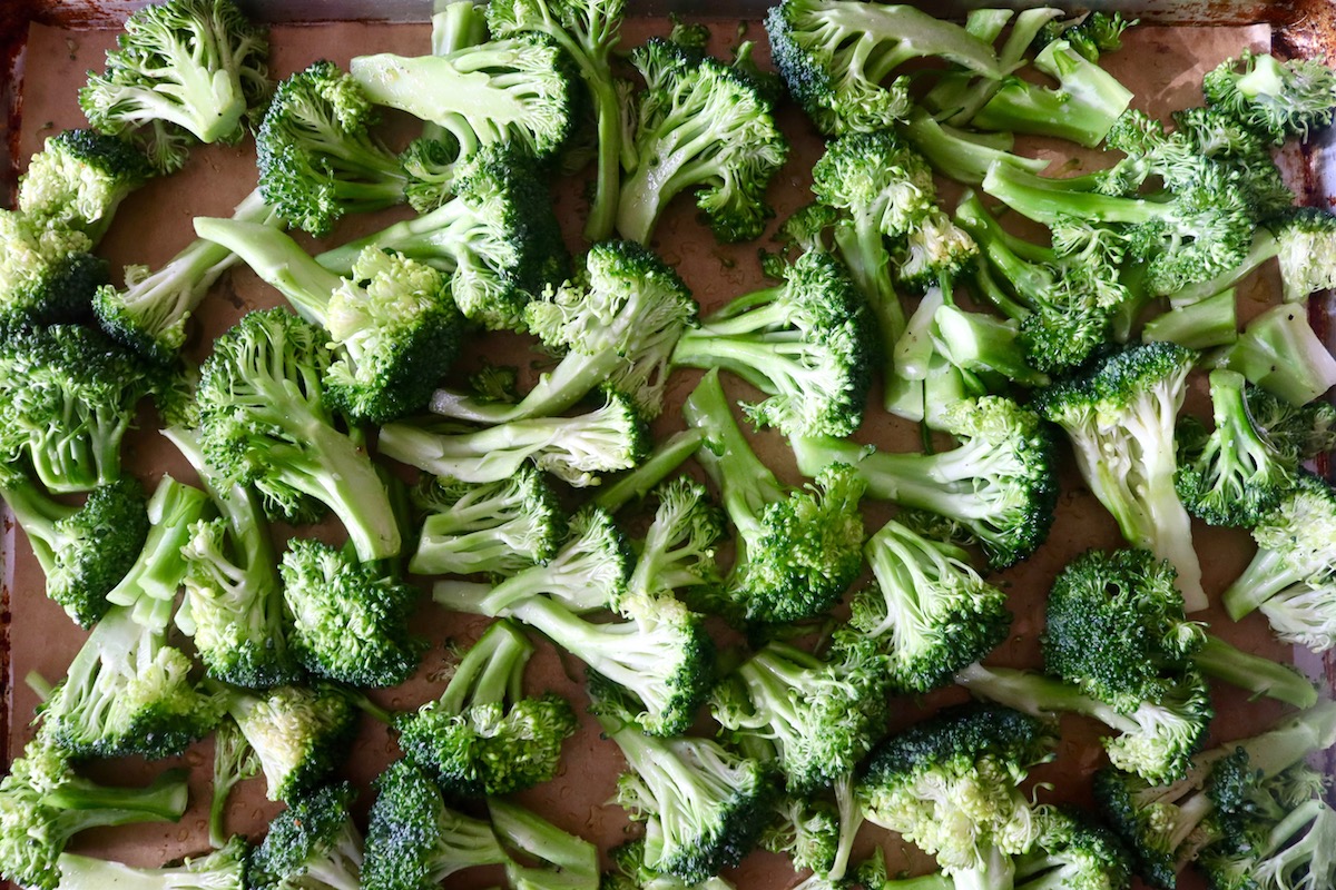 Raw pieces of broccoli on a parchment-lined baking sheet.