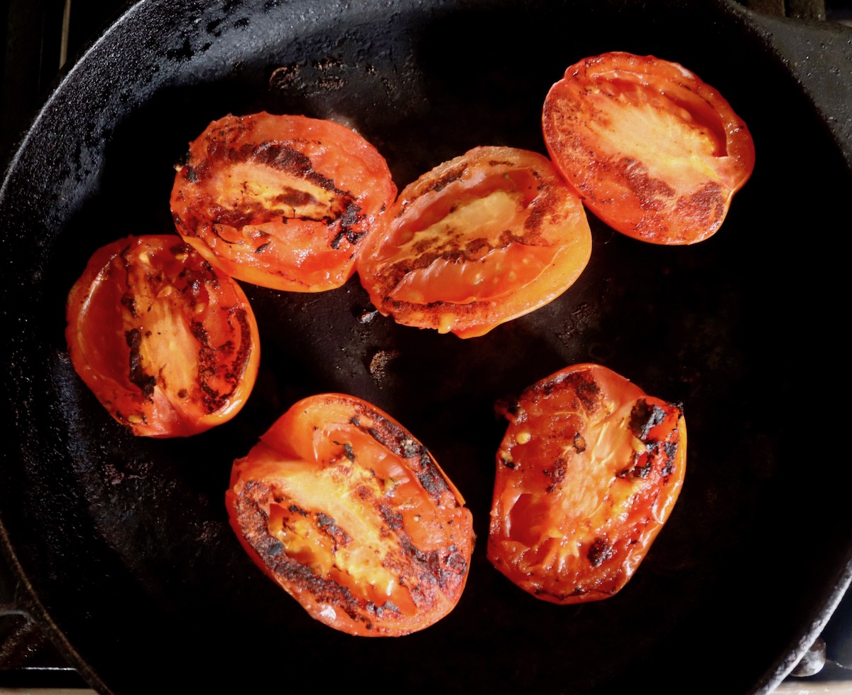 Blackened tomato halves in a cast iron skillet.