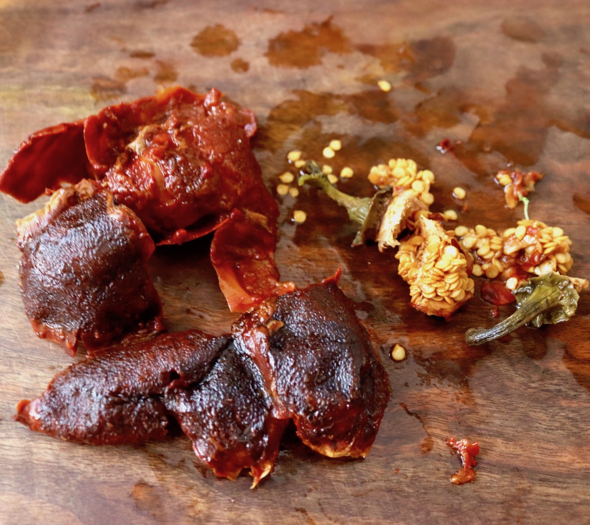 Hydrated dried red peppers on a dark wood cutting board with seeds and stems removed and next to them.
