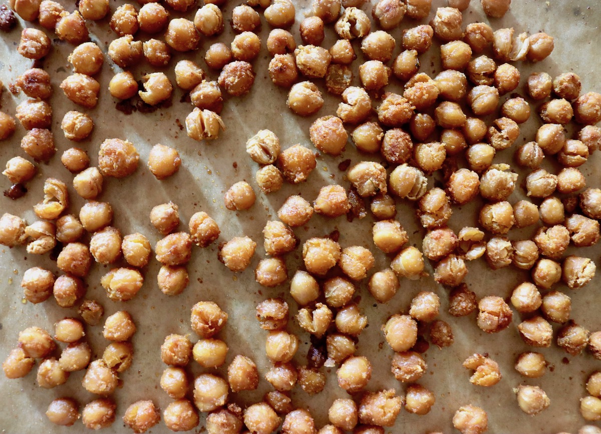 Roasted garbanzo beans with oil and spices on a parchment-lined baking sheet.