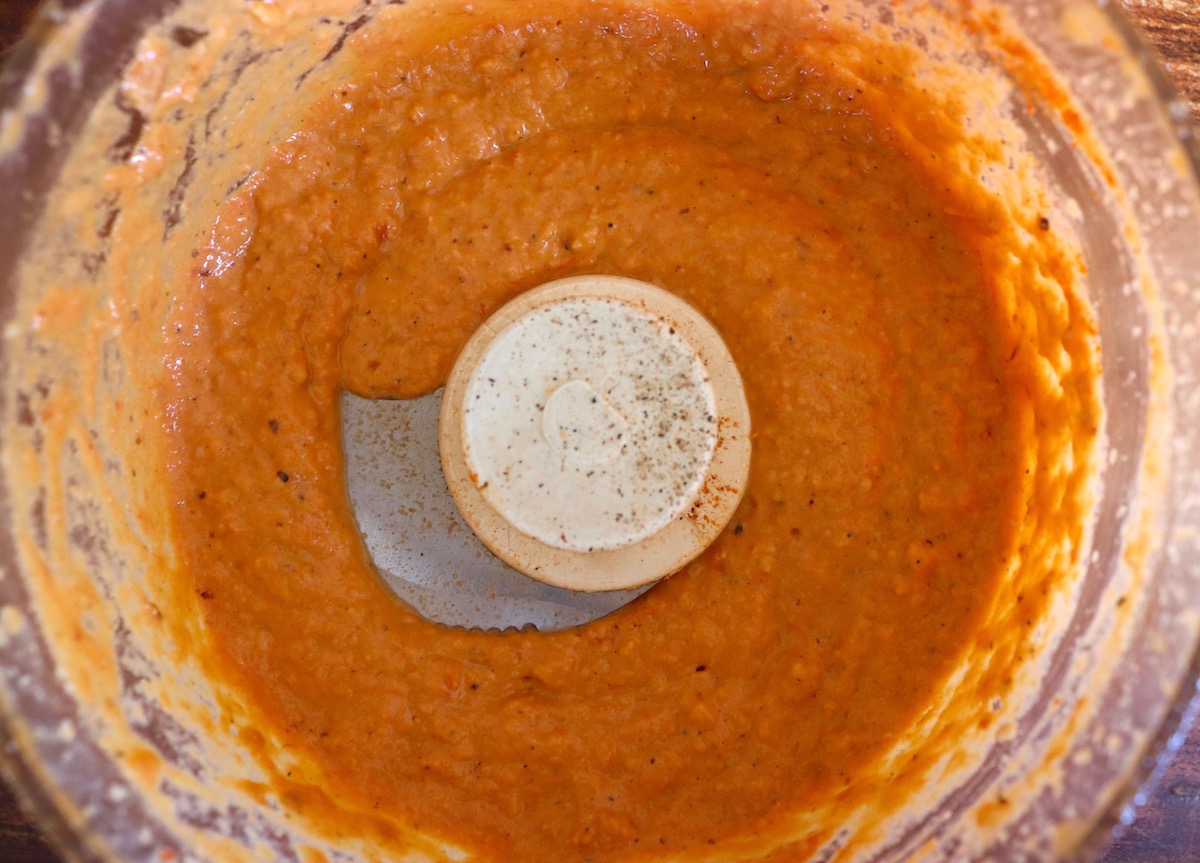 Orange-red Romesco sauce that's smooth and thick in a food processor bowl.