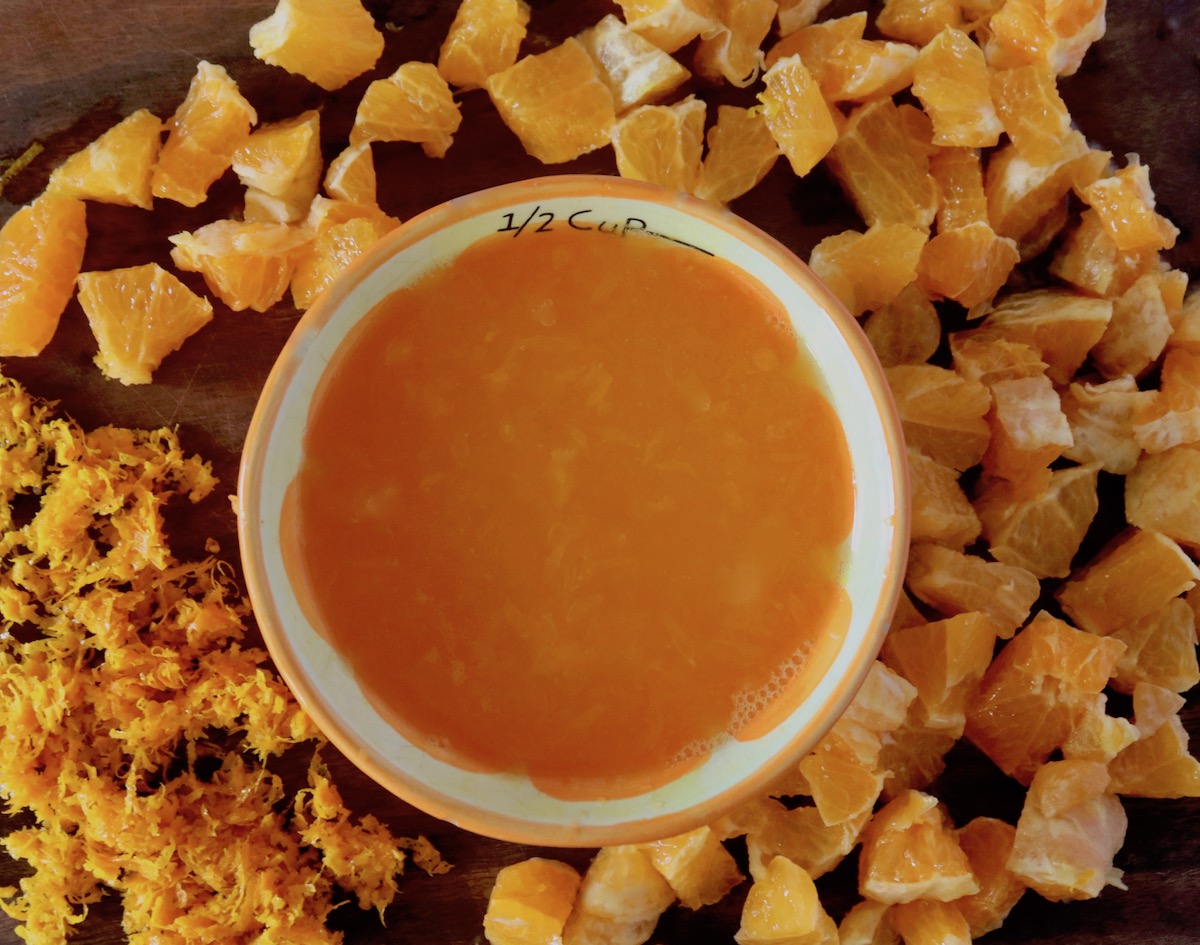 Chopped, zested and juice tangerines on a dark wood cutting board.