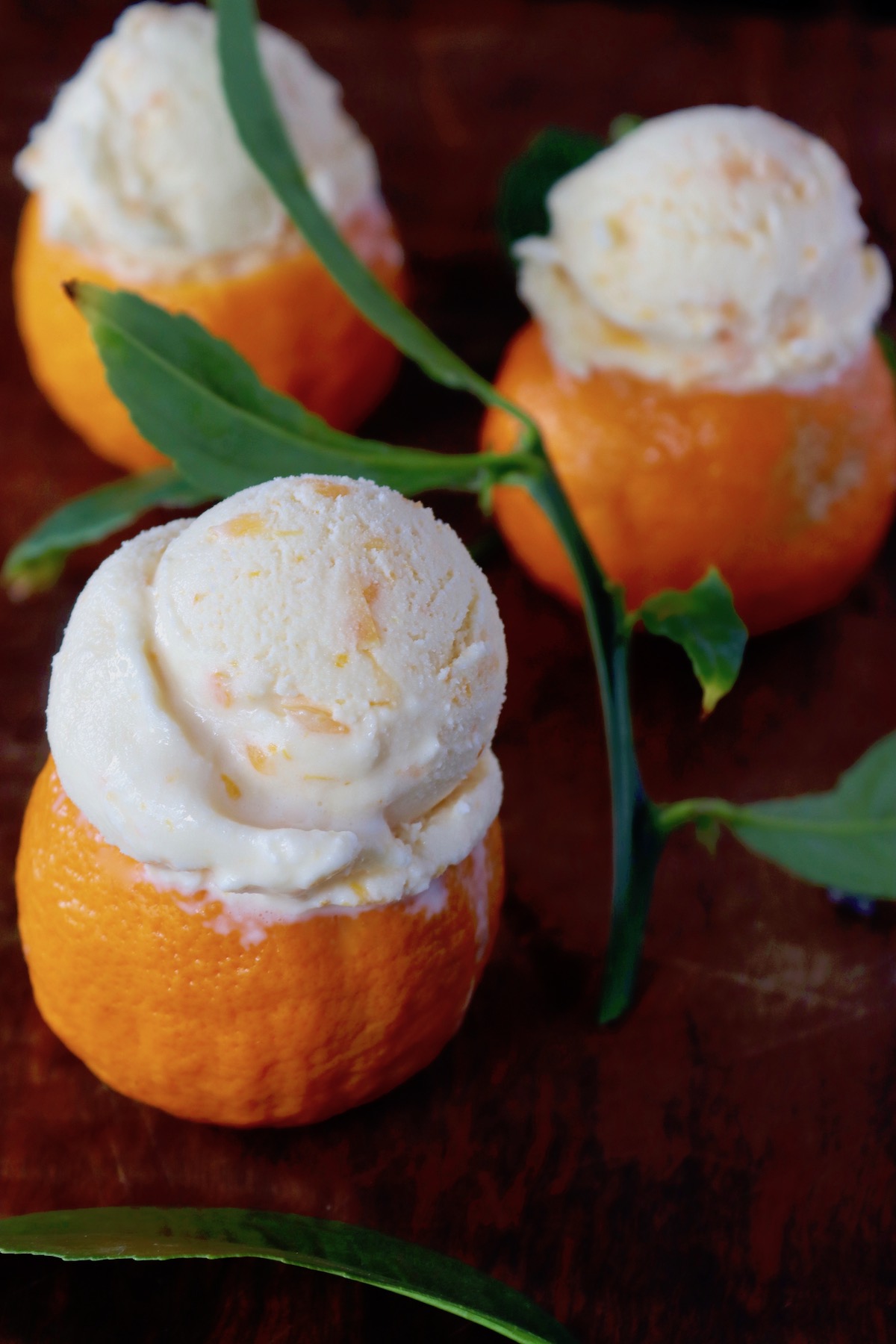 Three small bowls made of tangerines with creamsicle ice cream, on wood counter.