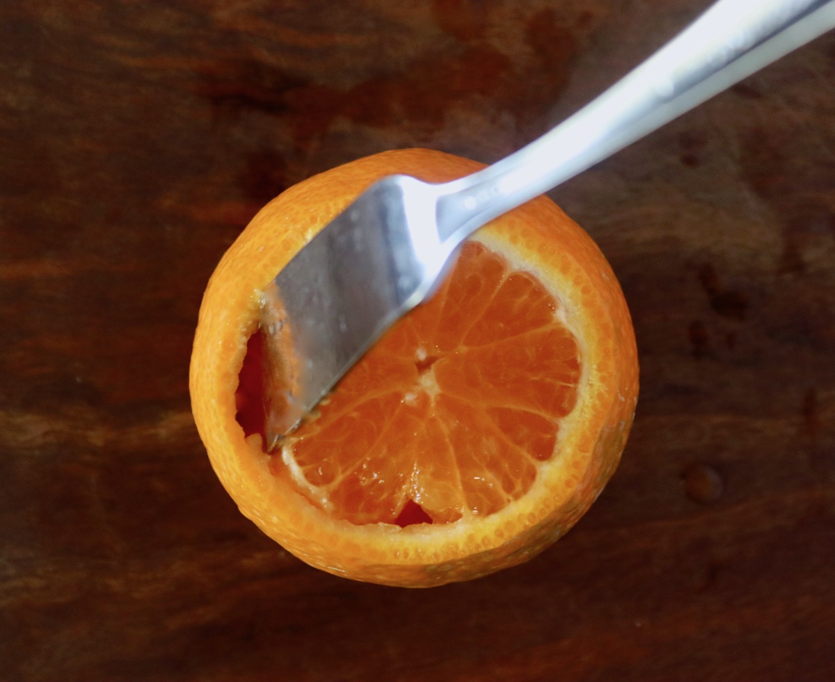 Tip of a butter knife cutting around citrus segments inside a tangerine.