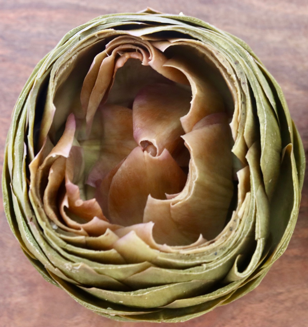 Top view of a steamed artichoke on a wooden surface.
