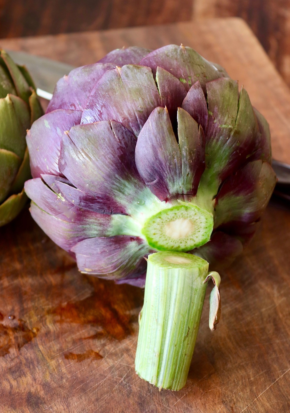 Purple artichoke with stem being cut off.