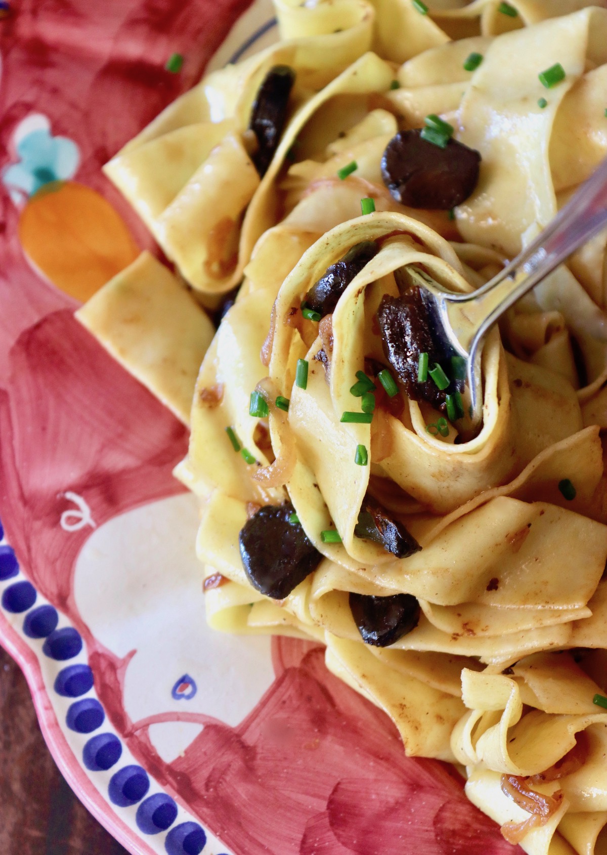 Ceramic, oval shaped, burgundy painted platter with Black Garlic Pappardelle pasta whapped around a large fork.